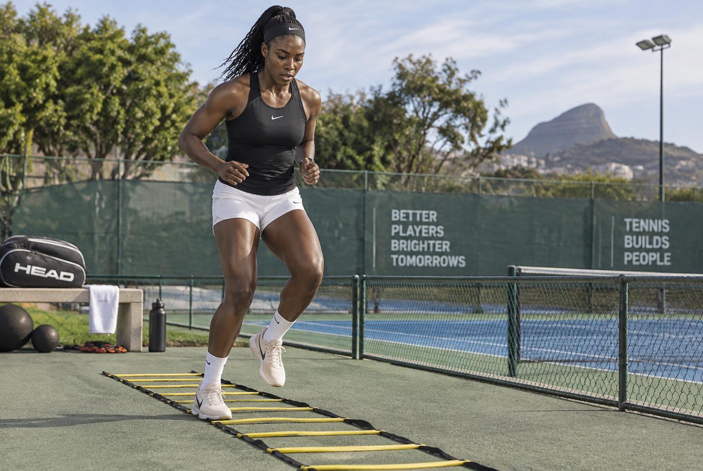 Black African tennis player performing agility conditioning beside a court